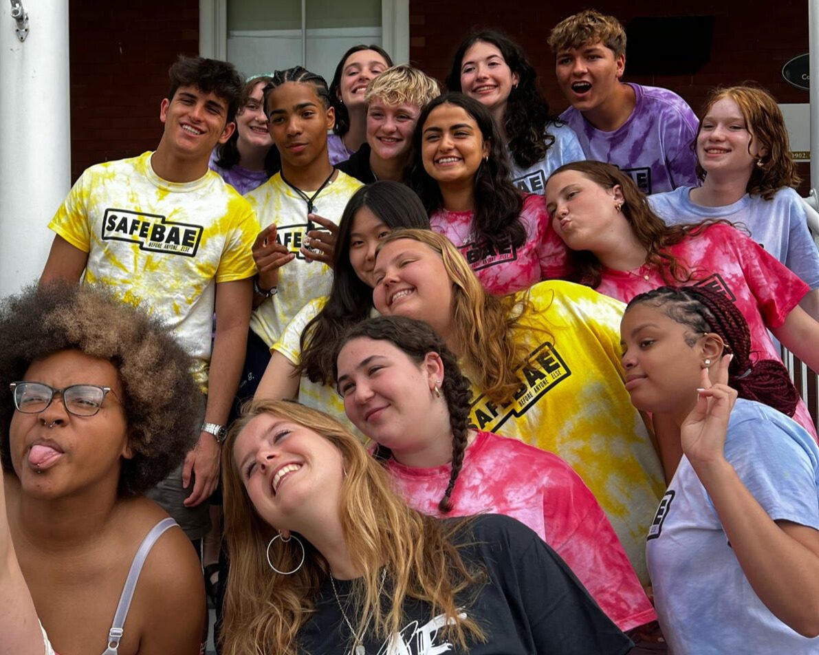Students in SafeBAE tie-dye shirts crowded together on a stoop, laughing